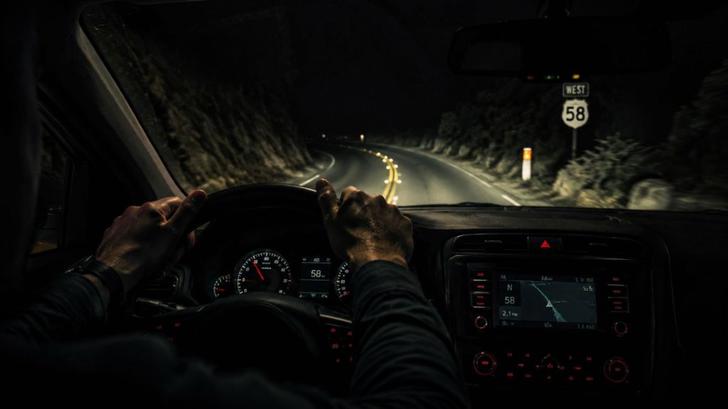 POV of a tired driver gripping a steering wheel on a dark road at night, representing the physical struggle of driving a vehicle with misaligned steering.